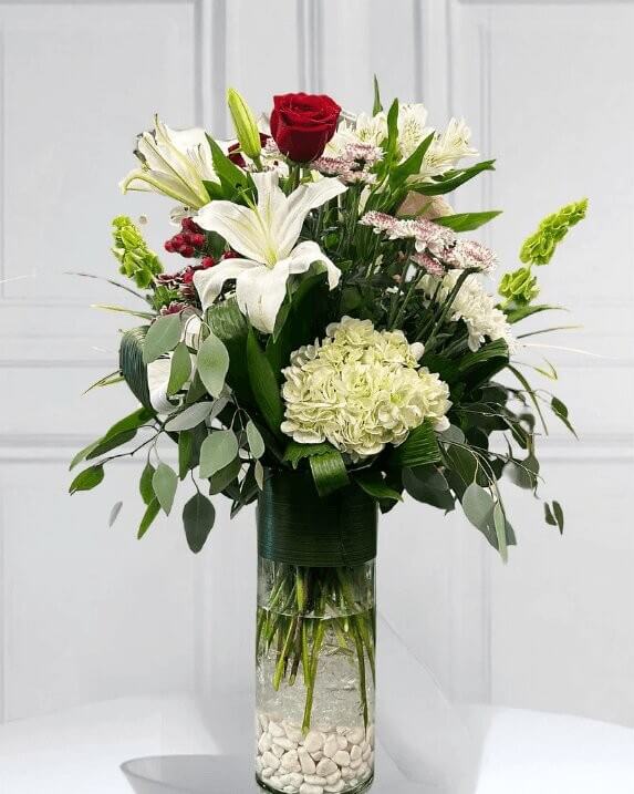 Arrangement floral blanc et vert avec une rose rouge dans un vase en verre – fleuriste Beloeil